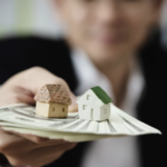 man in a classic suit hands out money with houses on it