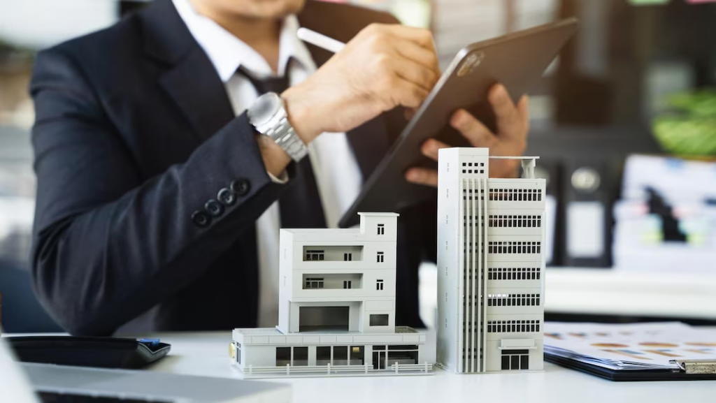 Man in a suit using a tablet with small houses on a table in front of him