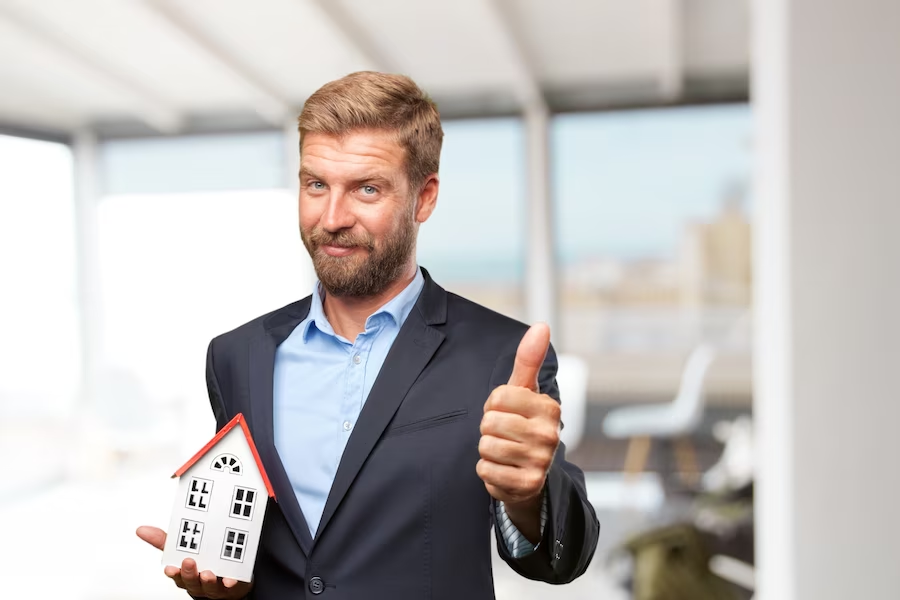 Man in suit giving a thumbs up while holding a tiny house