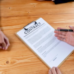 Two people facing each other at a table, one holding a contract and a pen