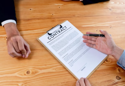 Two people facing each other at a table, one holding a contract and a pen