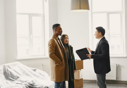 Three individuals conversing indoors in a newly furnished house with furniture still covered