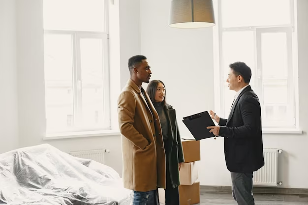 Three individuals conversing indoors in a newly furnished house with furniture still covered