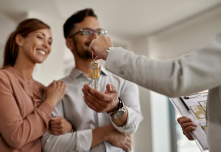 person passing keys to a smiling couple of woman and man